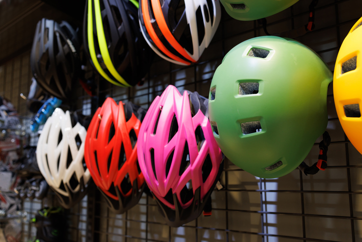 Bicycle safety helmets hang on metal wall in a bike shop.